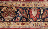 A weaver's insignia above the navy blue border with scrolling tendrils and floral palmettes.