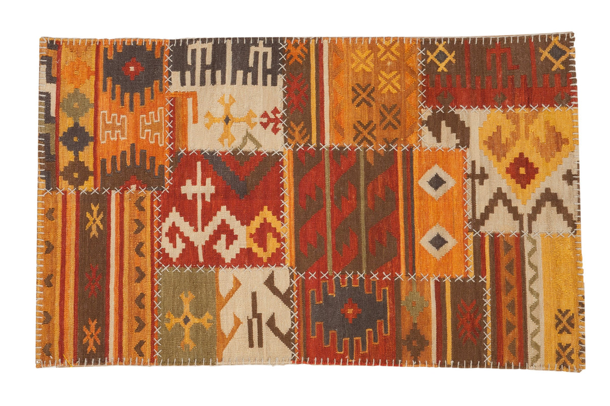 Patchwork kilim rug with geometric panels in warm orange, red, and brown, joined by white cross-stitching.