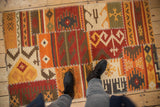 Warm patchwork kilim rug with brick red, orange, ivory, brown panels, white cross-stitches.