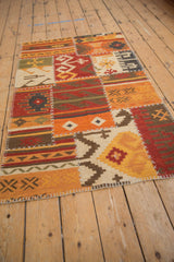 Kilim rug detail: geometric patchwork panels in red, orange, ivory, with visible raised cross-hatch stitches.