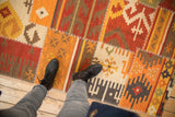 Handwoven kilim rug featuring patchwork panels, white cross-hatch stitches, and warm geometric patterns.