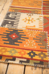 Close-up of warm-toned patchwork kilim rug, highlighting simulated cross-stitch seams and geometric panels.