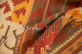 Warm patchwork kilim rug with primitive geometric panels and white cross-hatch stitching.