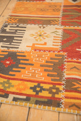 Detail of geometric patchwork kilim rug with warm orange, red panels, cross-hatch stitches.