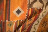 Detail of patchwork Kilim rug with white cross-stitching and warm geometric panels.