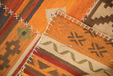 Patchwork kilim rug featuring white cross stitches joining orange, red, and brown panels.