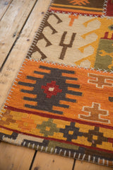 Close-up of geometric kilim runner's stitched patchwork panels in orange, brown, ivory, and olive.