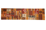 A long patchwork Kilim runner with stitched geometric panels in warm shades of red, orange, and brown.