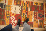 A person's view of the patchwork kilim's warm geometric patterns and raised cross-hatch stitching.