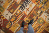 Warm-toned patchwork kilim with geometric guls, rams horn motifs, and white cross-hatch stitching.