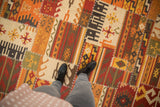 Warm palette patchwork Kilim rug, highlighting finned floral guls, rams horn motifs, and cross-stitch seams.