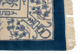 Plush ivory Peking rug corner: blue floral and geometric patterns, indigo border, stain, irregular fringe.