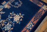 Corner of vintage Peking rug with ivory blossoms, blue leaves, and terra cotta geometric border.