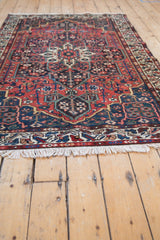 Vintage Persian Baktiari rug viewed from a low angle, showing the fringe and brick red medallion pattern.
