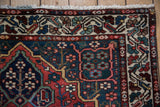 A vintage Persian Baktiari rug corner, showing the floral main border and white knotted fringe.