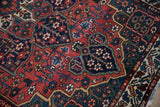 Evenly worn pile on a vintage Bakhtiari rug showing intricate buds and vines in red and navy.