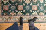 Close-up of vintage Indian rug with green floral field and blush, blue geometric border.