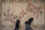 Expressive mauve dragon motif with cloudbands on ivory Peking rug, showing embossed pile and black boots.
