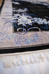Art Deco rug corner: platinum floral border, charcoal field, denim blue, and clean white fringe.