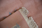 Corner of vintage Art Deco rug, showing thick dusty rose pile, ivory fringe, and woven foundation.
