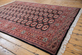Angled corner view of a vintage Bokhara rug showing the intricate borders and plush pile.
