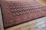 Angled view of a vintage Bokhara carpet's lustrous wool pile and repeating geometric gul pattern.