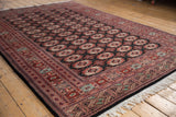 Angled view of a vintage Bokhara carpet showing the geometric border, lustrous pile, and ivory fringe.