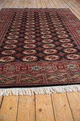 Low angle on a vintage Bokhara carpet showing its plush pile and repeating gul medallions.