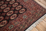 Angled corner view of a fine Bokhara carpet, showing the plush pile, detailed border, and intact ivory fringe.