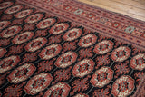 Angled view of a Bokhara carpet's intricate geometric border and repeating gul motifs.