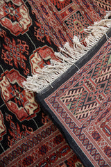 Folded corner of a Bokhara rug revealing the hand-knotted back, full pile, and ivory fringe.