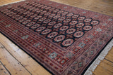 Detailed geometric gul medallions and ornate borders on a vintage Bokhara carpet in navy, brick red, and ivory.