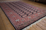 Vintage Bokhara rug corner showing ivory fringe and black selvage with geometric border.