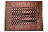 A vintage fine Bokhara carpet with repeating rust and ivory gul medallions on a black background.