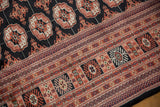 Detailed view of a fine Bokhara's intricate geometric border and plush, black field with rust guls.
