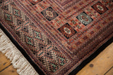 Neatly finished corner of a vintage Bokhara carpet with full ivory fringe and geometric borders.