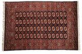 Vintage Bokhara carpet with repeating rust and ivory gul medallions on a black field and geometric borders.