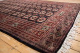Corner detail of a vintage Bokhara carpet highlighting the intricate geometric border, dark selvage, and plush pile.