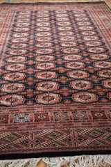 Close view of a vintage Bokhara's plush pile, intricate geometric border, and clean white fringe.