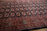 Low-angle detail of a Bokhara carpet's plush pile and intricate rust and black border.