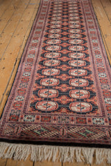 Long perspective of a vintage Bokhara runner with rust and ivory gul medallions on a black field.