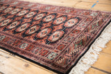 Angled view of a vintage Bokhara runner highlighting its plush pile, border, and ivory fringe.