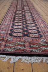 Bokhara runner with brick red, antique ivory gul medallions on dark navy field, and white fringe.