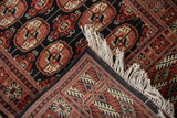 Bokhara rug corner showing tight geometric back weave, ivory fringe, and plush rust medallions.