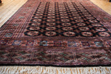 Perspective view of a vintage Bokhara carpet, focusing on the intricate border, ivory fringe, and soft wool.