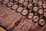 Intricate geometric border and plush charcoal wool pile of a vintage hand-knotted Bokhara carpet.