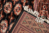 Folded corner of a vintage Bokhara rug showing its dense pile, detailed back, and ivory fringe.