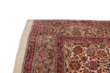 Vintage Kerman carpet corner showcasing ivory fringe, cochineal red border, and floral vine palmettes.