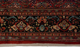 Floral blossoms and serrated leaves on the intricate navy border of a vintage Persian Mahal carpet.