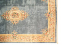 Denim blue Savonnerie rug corner with ivory border, floral vinery, and fringe.